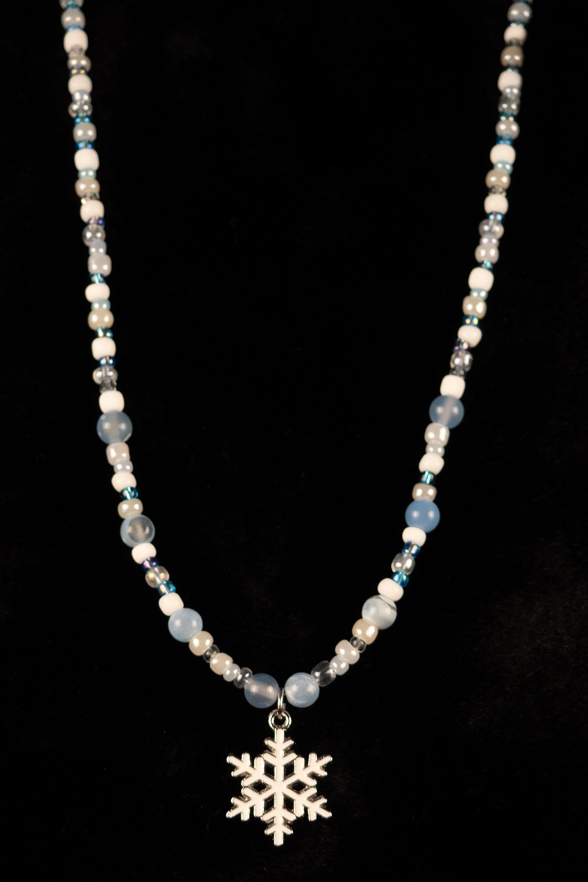 Blue and white beaded necklace with snowflake pendant on a black background