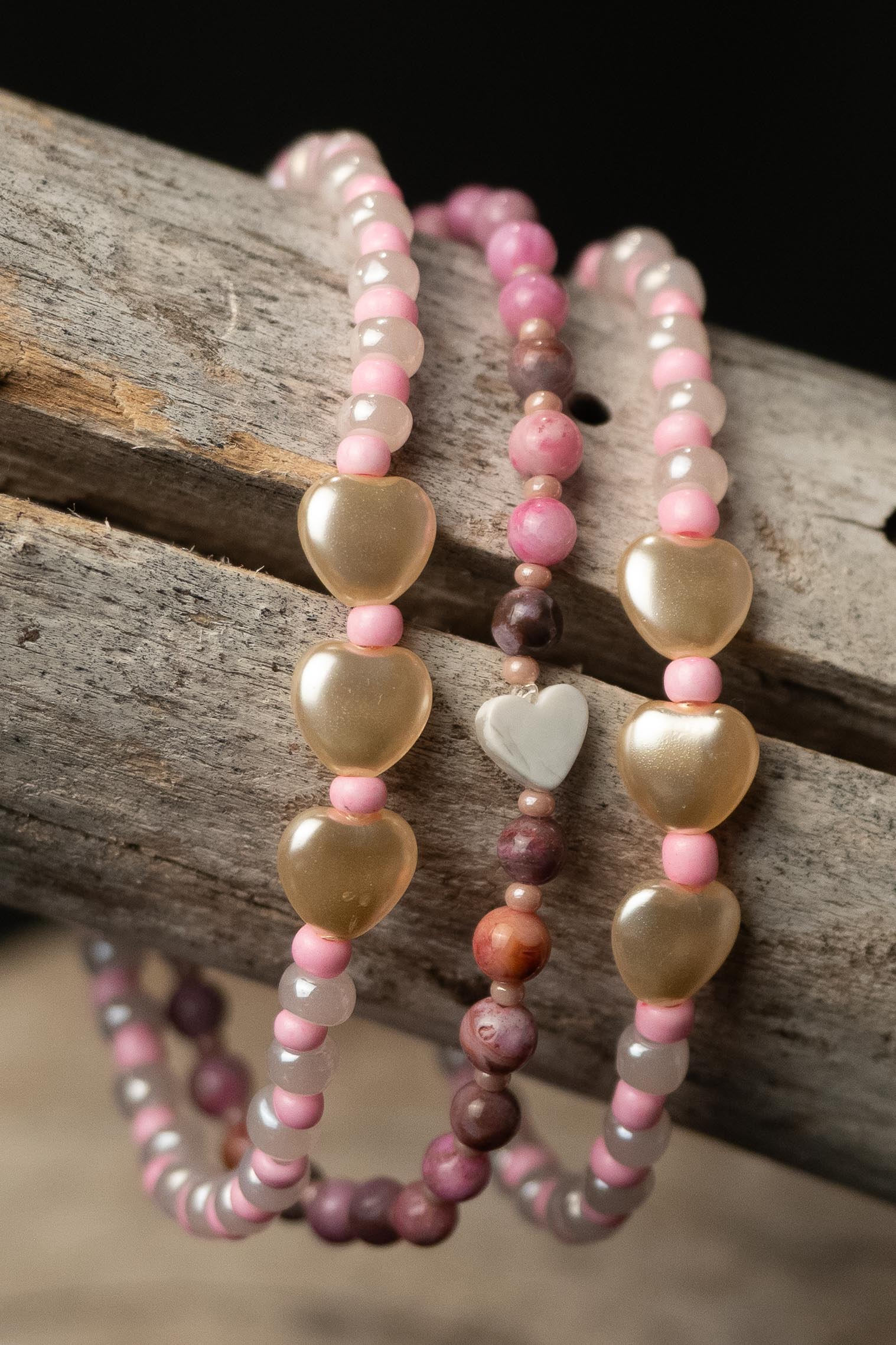 Three pink and purple beaded bracelets with heart-shaped beads on a wooden surface