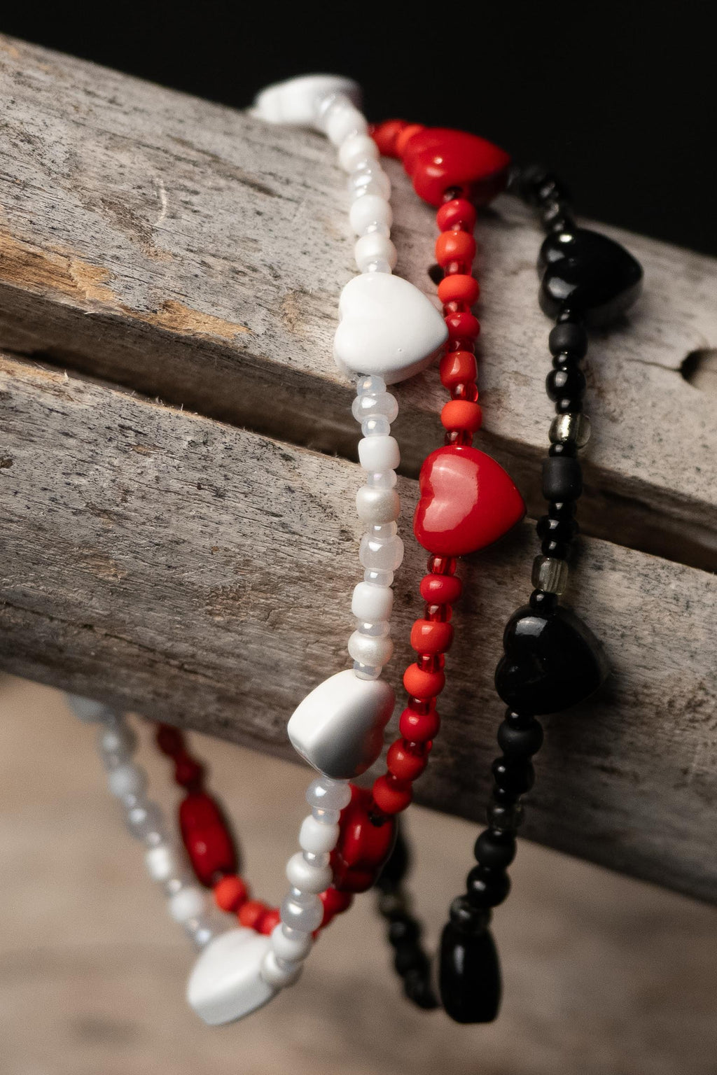 Three beaded bracelets in white, red, and black with hearts on a wooden surface.