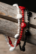 Three beaded bracelets in white, red, and black with hearts on a wooden surface.
