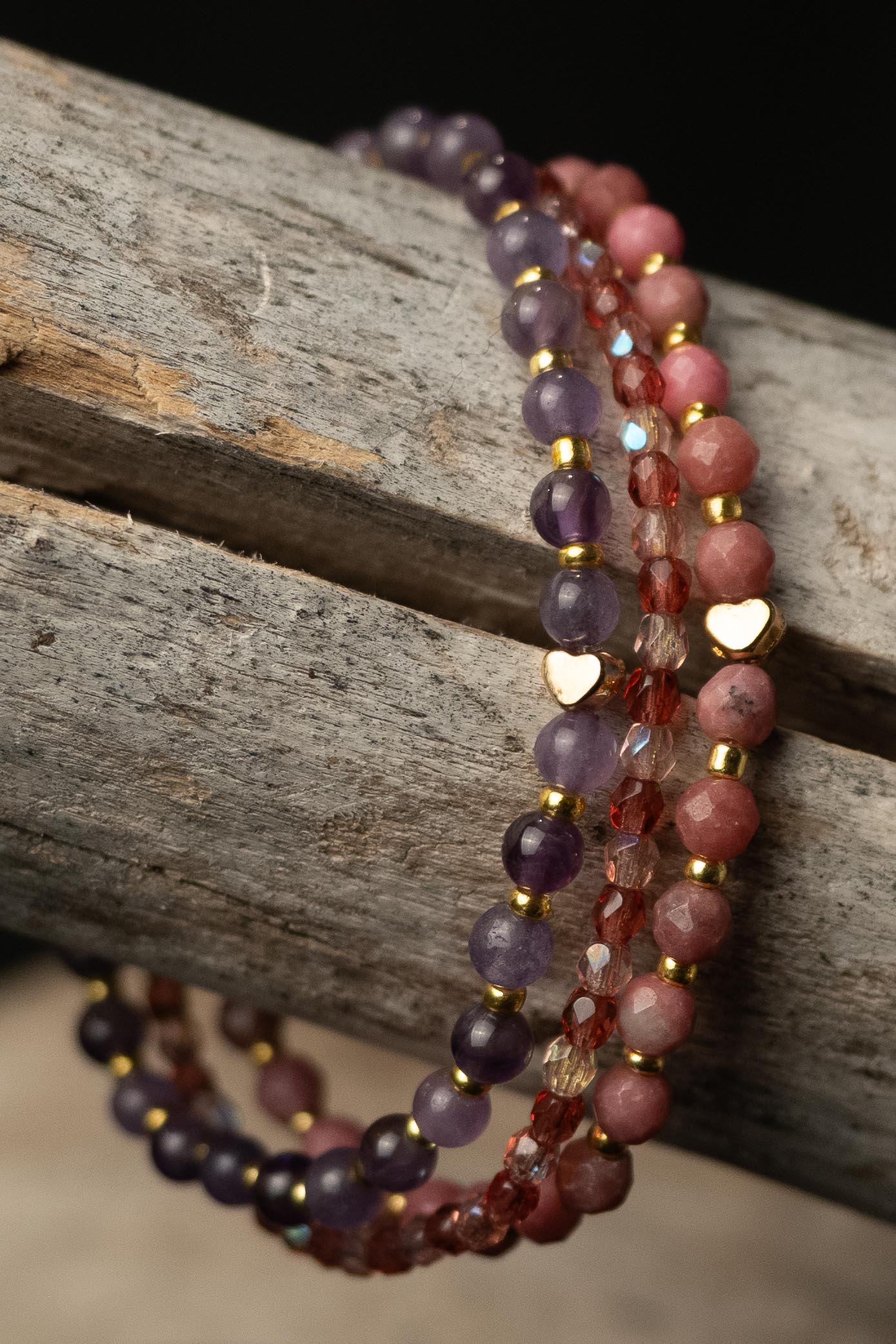 Stack of purple, pink, and clear beaded bracelets with tiny gold hearts on a wooden surface