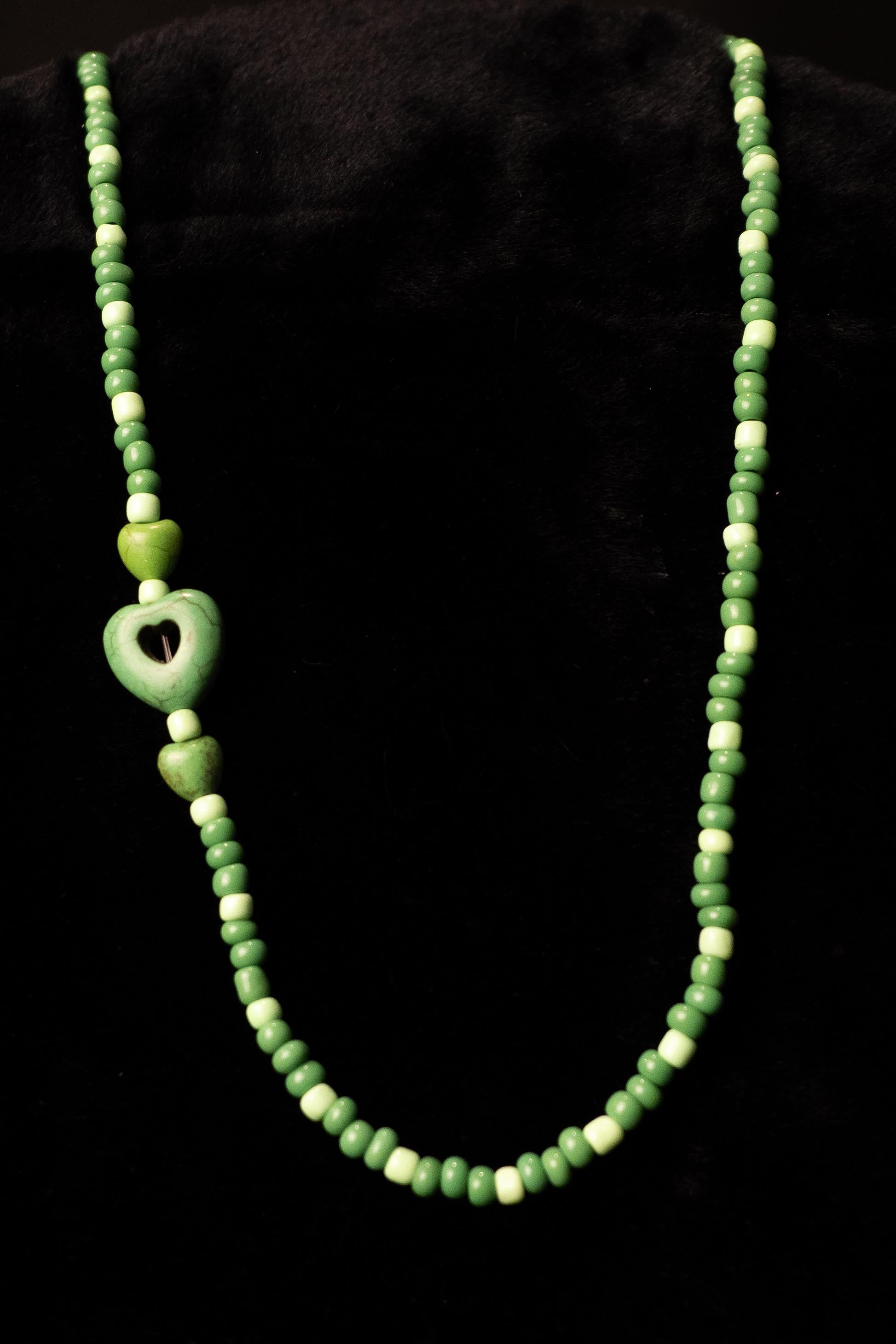 Green beaded necklace with  heart-shaped pendants on a black background