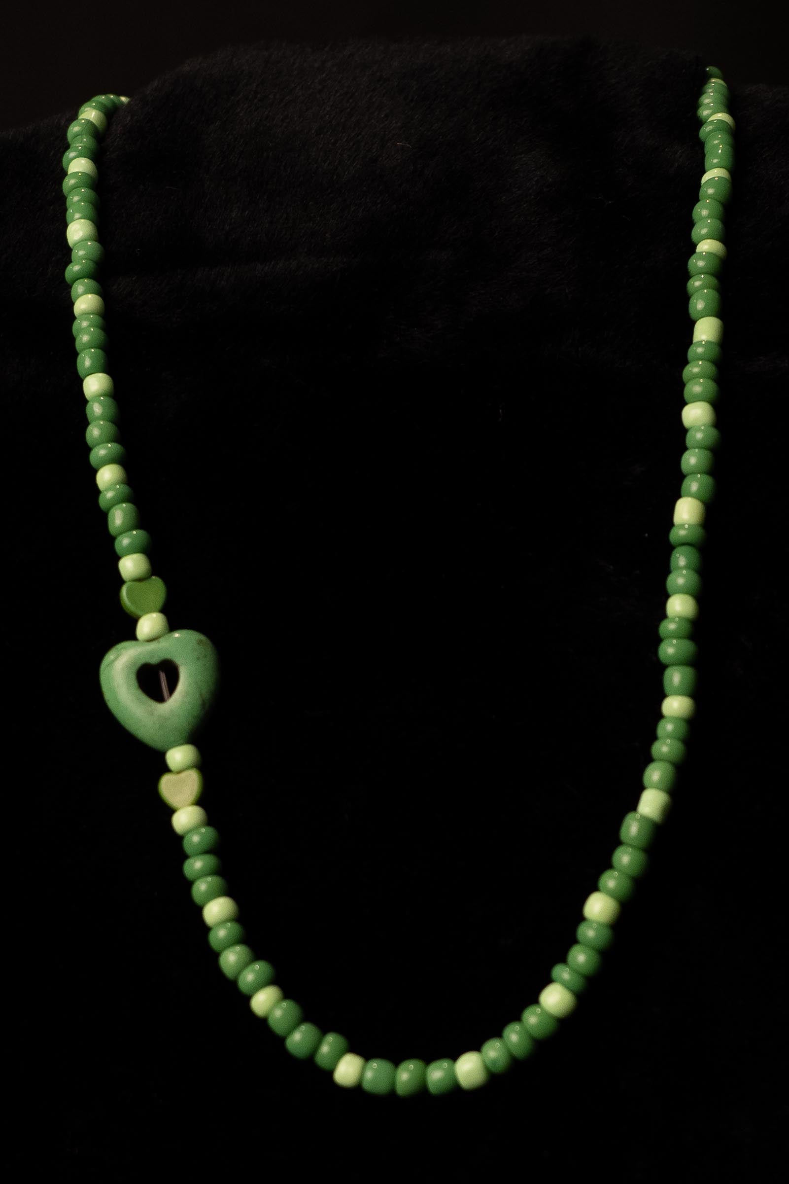 Green beaded necklace with heart-shaped pendants on a black background