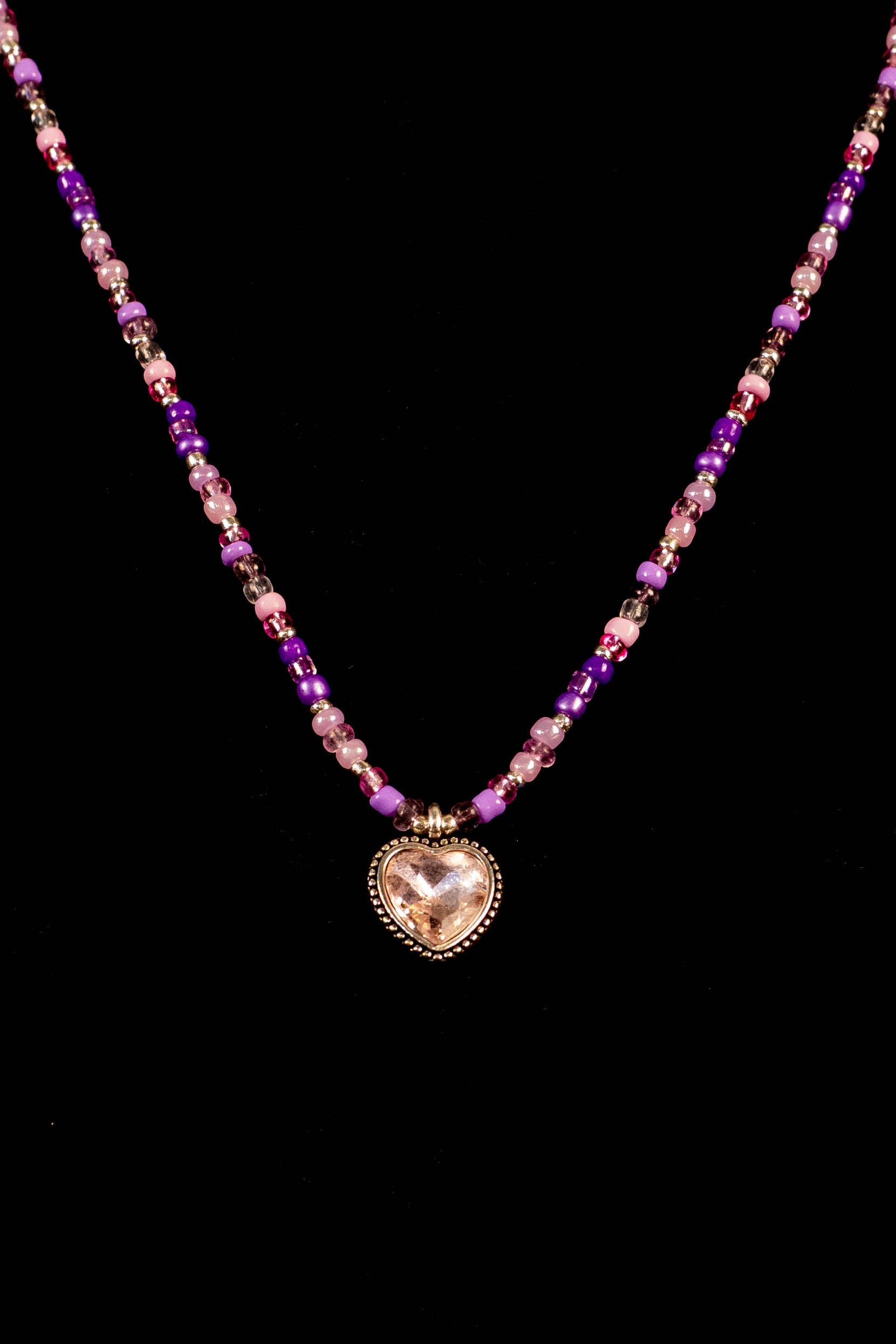 Necklace with heart-shaped pendant and purple multicolored beads on a black background