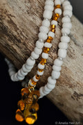 Three beaded bracelets with white beads and orange accents with a gummy-bear charm on a wooden surface.