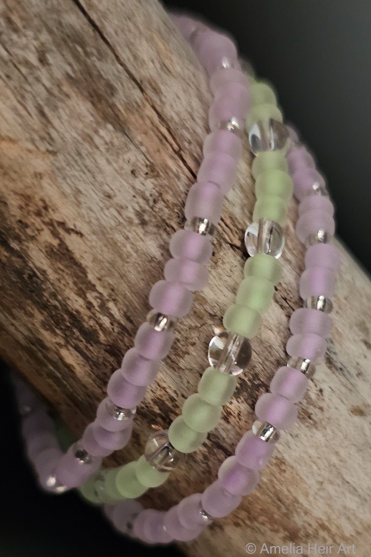 Three beaded bracelets in purple and green glow-in-dark beads on a wooden surface