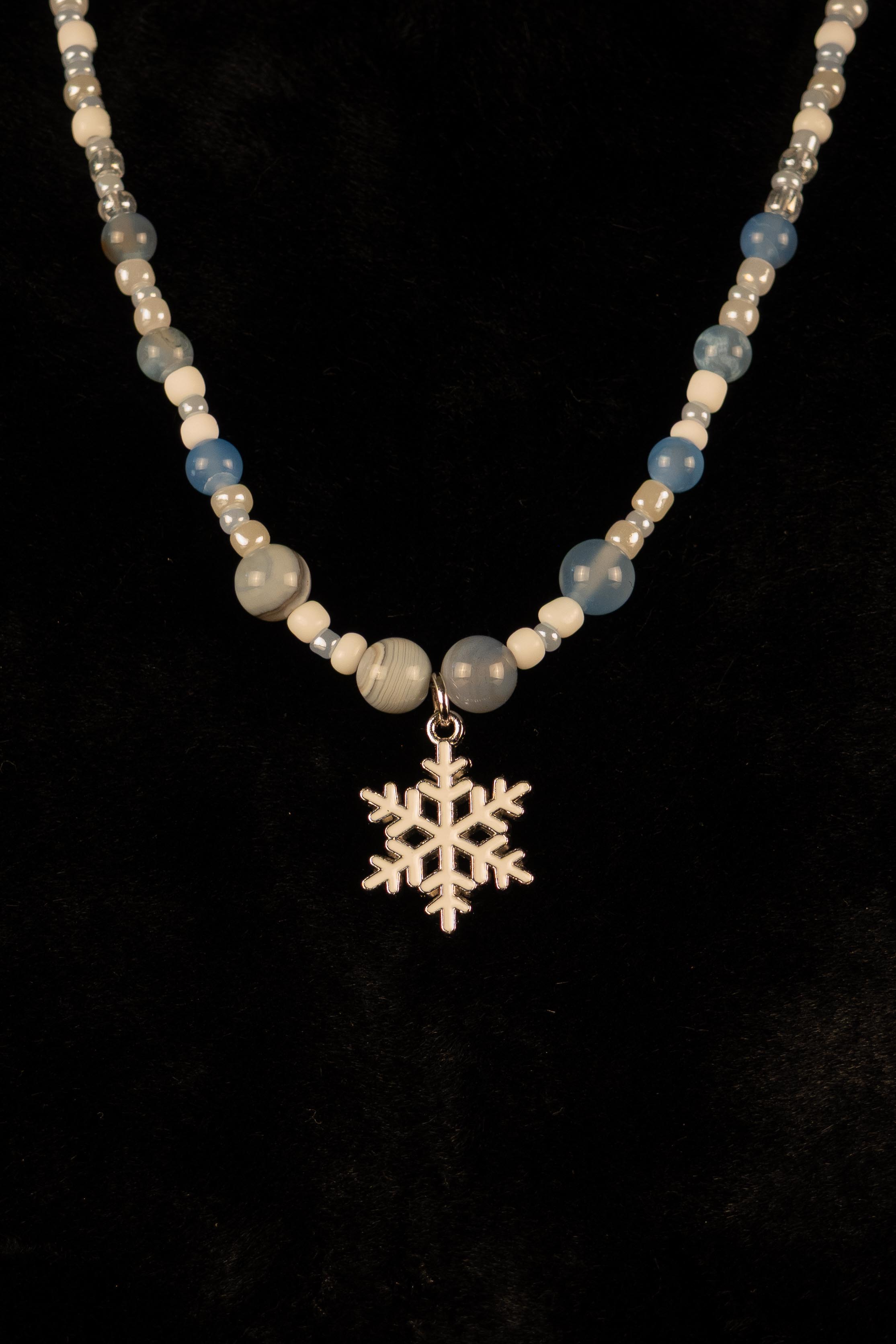 Blue and white necklace with snowflake pendant on a black background