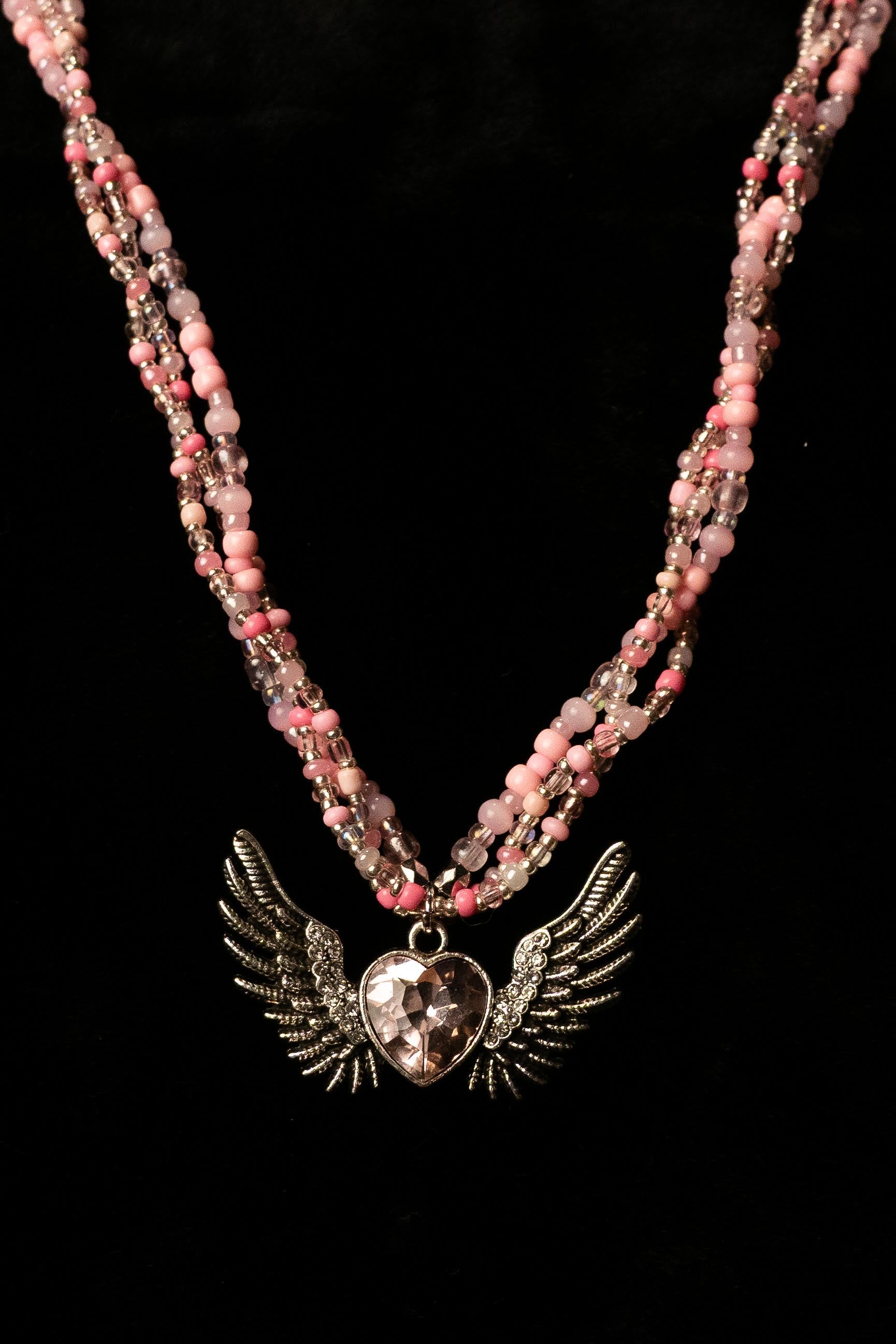 Three strand necklace with pink beads and a heart pendant with wings on a black background