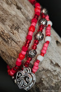 Red, pink, and white beaded bracelet with silver rose shaped beads silver heart charms on a wooden surface