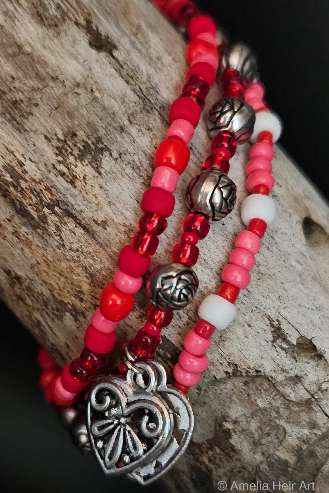 Red, pink, and white beaded bracelet with silver rose shaped beads silver heart charms on a wooden surface