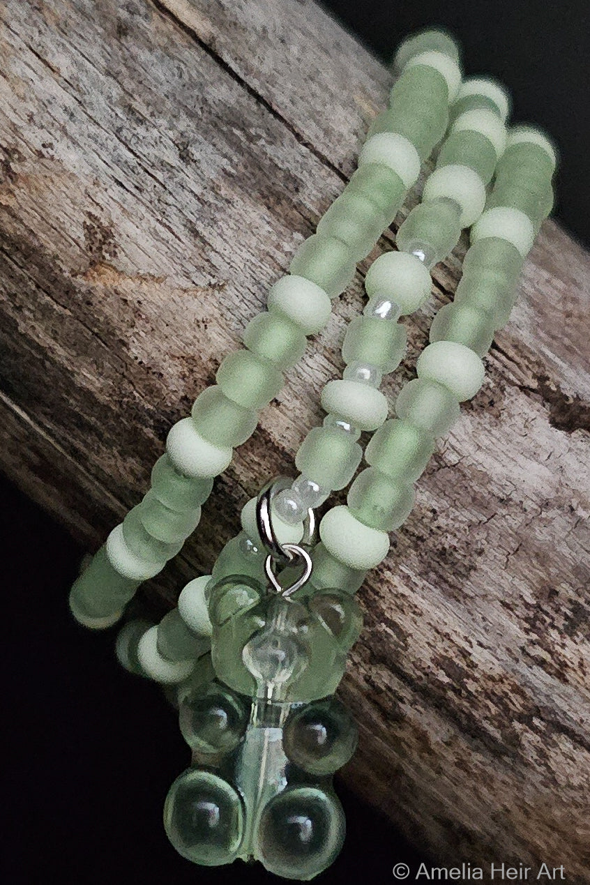 Green beaded bracelets with a gummy-bear-shaped charm on a wooden surface