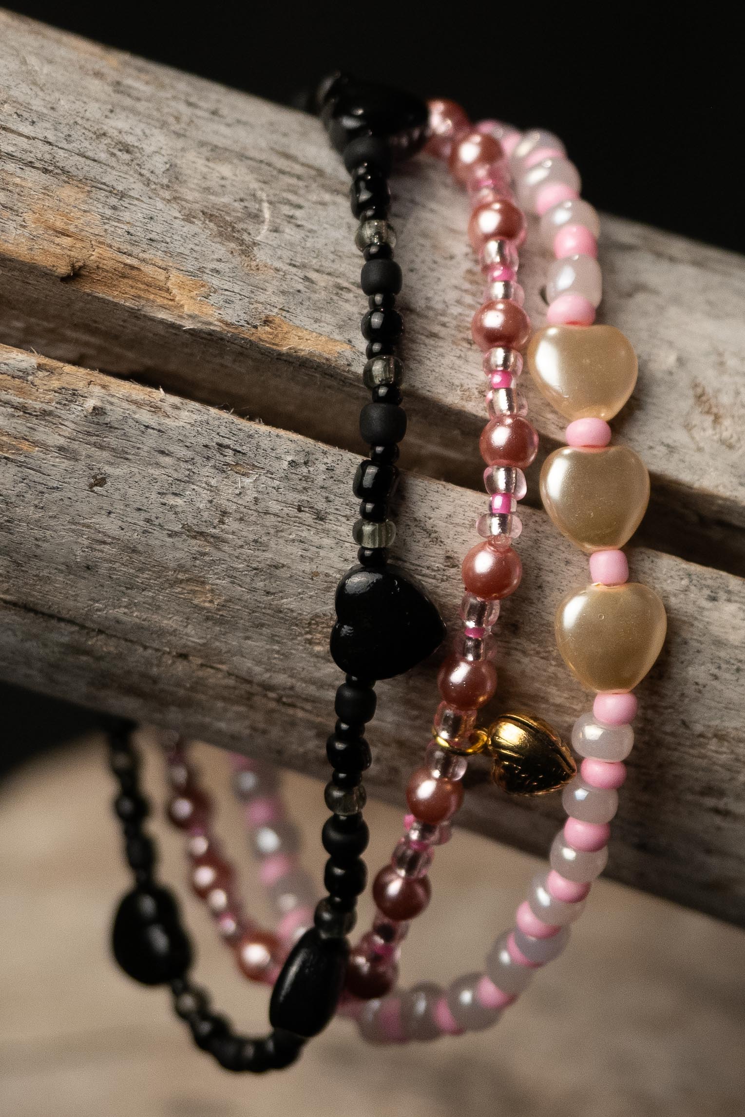 Set of black, pink, and cream beaded bracelets with hearts on a wooden surface