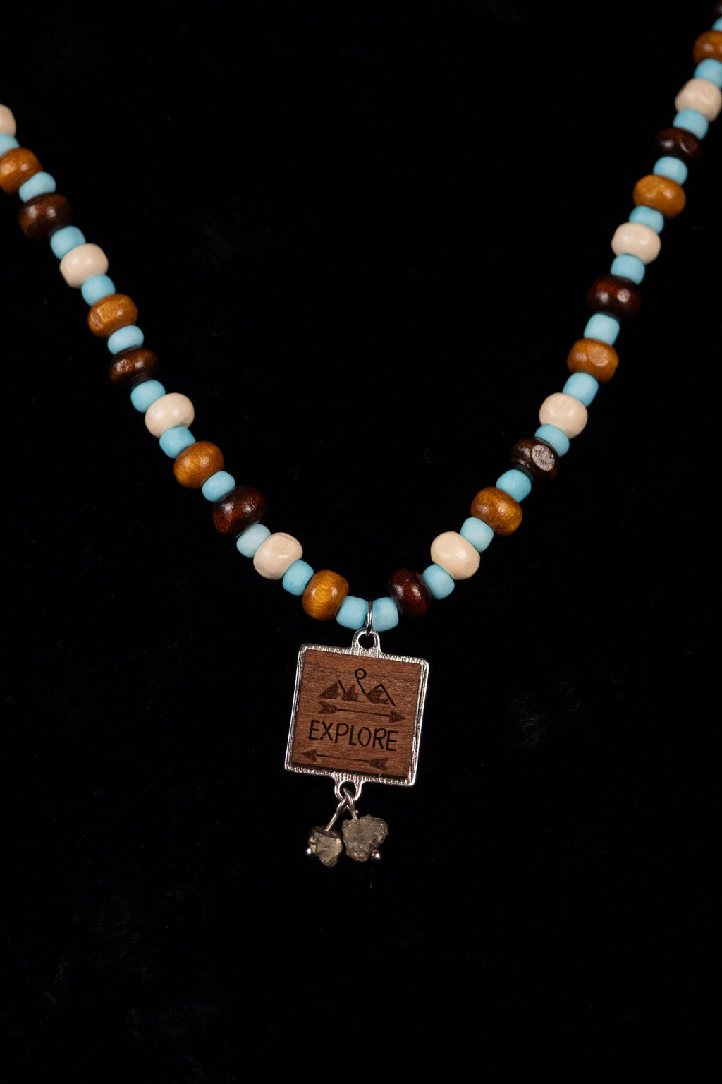 Explore handcrafted wood, cream, brown, blue & fool's gold beaded necklace with EXPLORE pendant on a black background — Amelia Heir Art