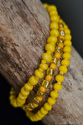 Three yellow beaded bracelets on a wooden surface