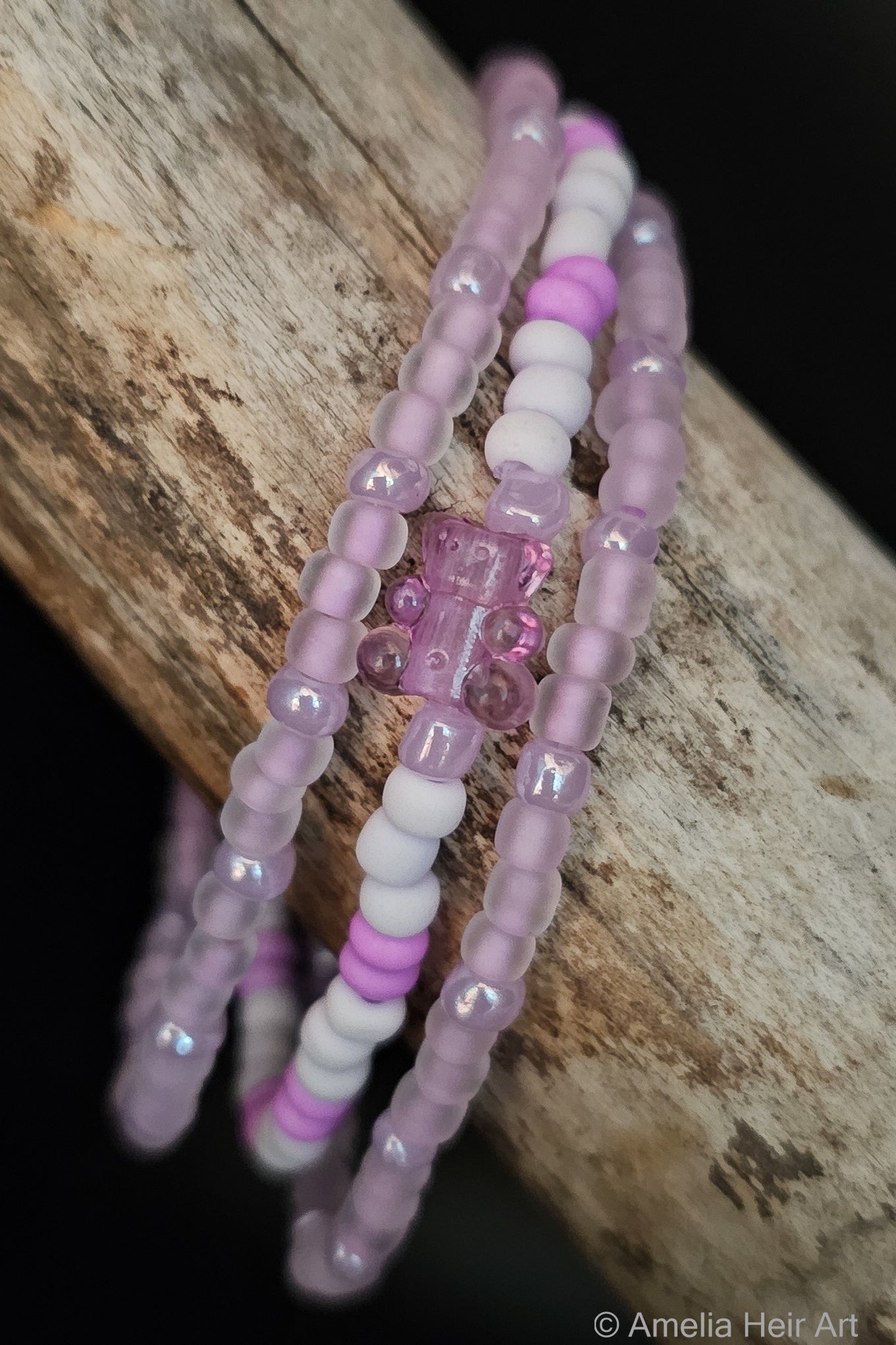 Set of beaded bracelets with glow-in-the-dark purple beads with a gummy-bear-shaped bead on a wooden surface