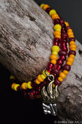 Red, orange, yellow, and brown beaded bracelet with a metal fire and logs charm on a wooden surface