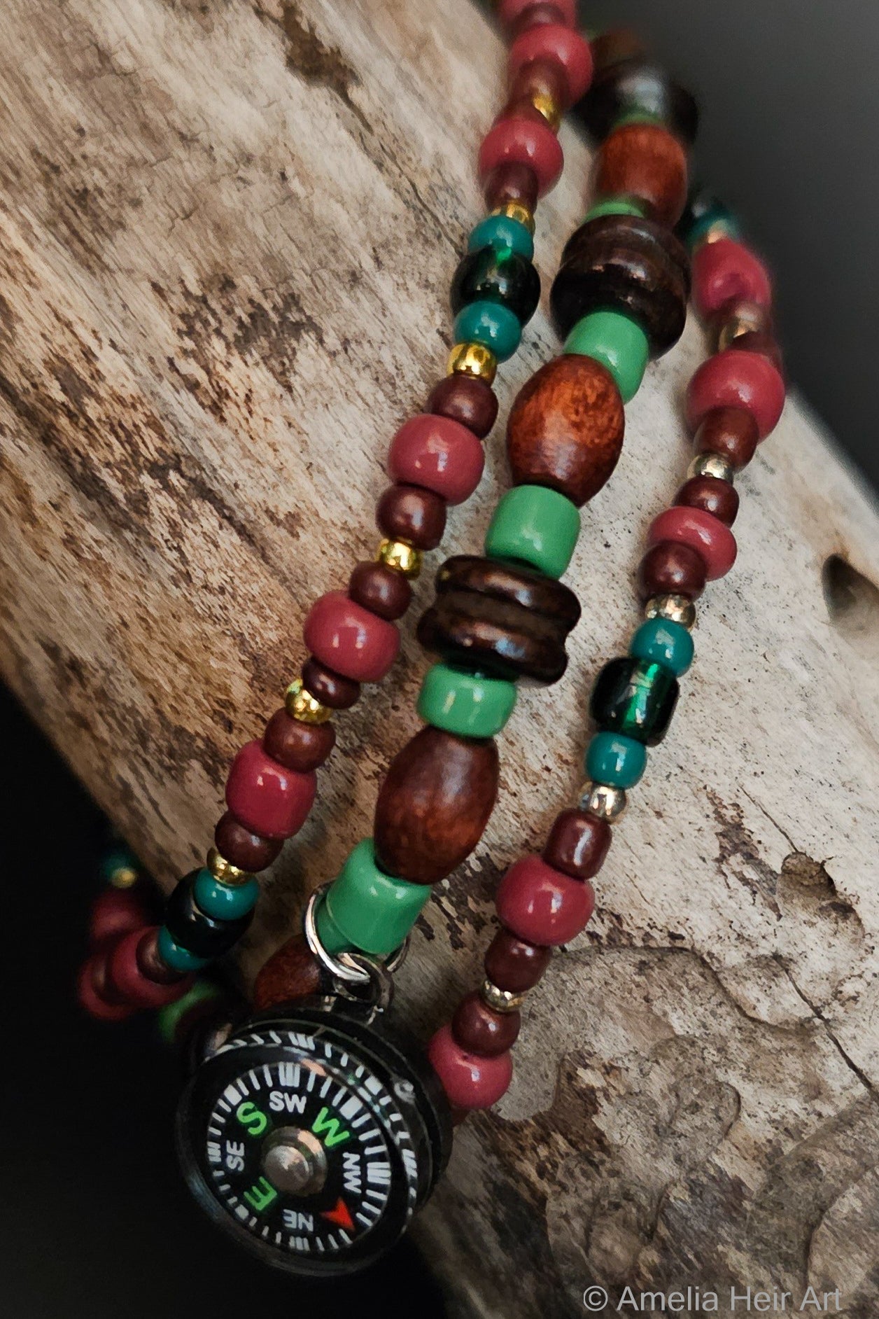 Green and brown beaded bracelets with a compass charm on a wooden surface