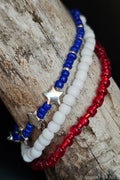 Three beaded bracelets in blue, white, and red on a wooden surface.