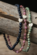 Set of navy, pink, and turquoise beaded bracelets with white heart-shaped beads on a wooden surface