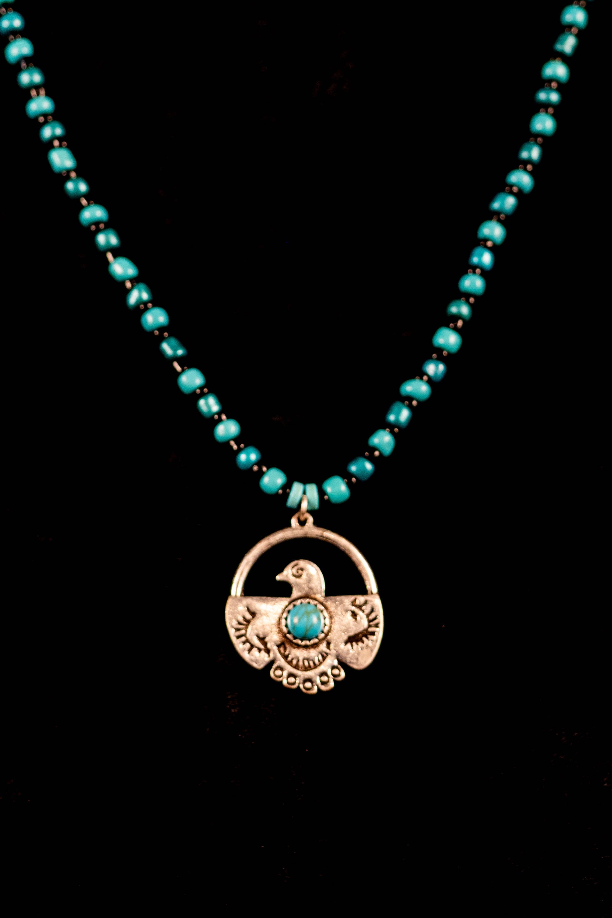 Necklace with turquoise beads and a silver eagle pendant on a black background