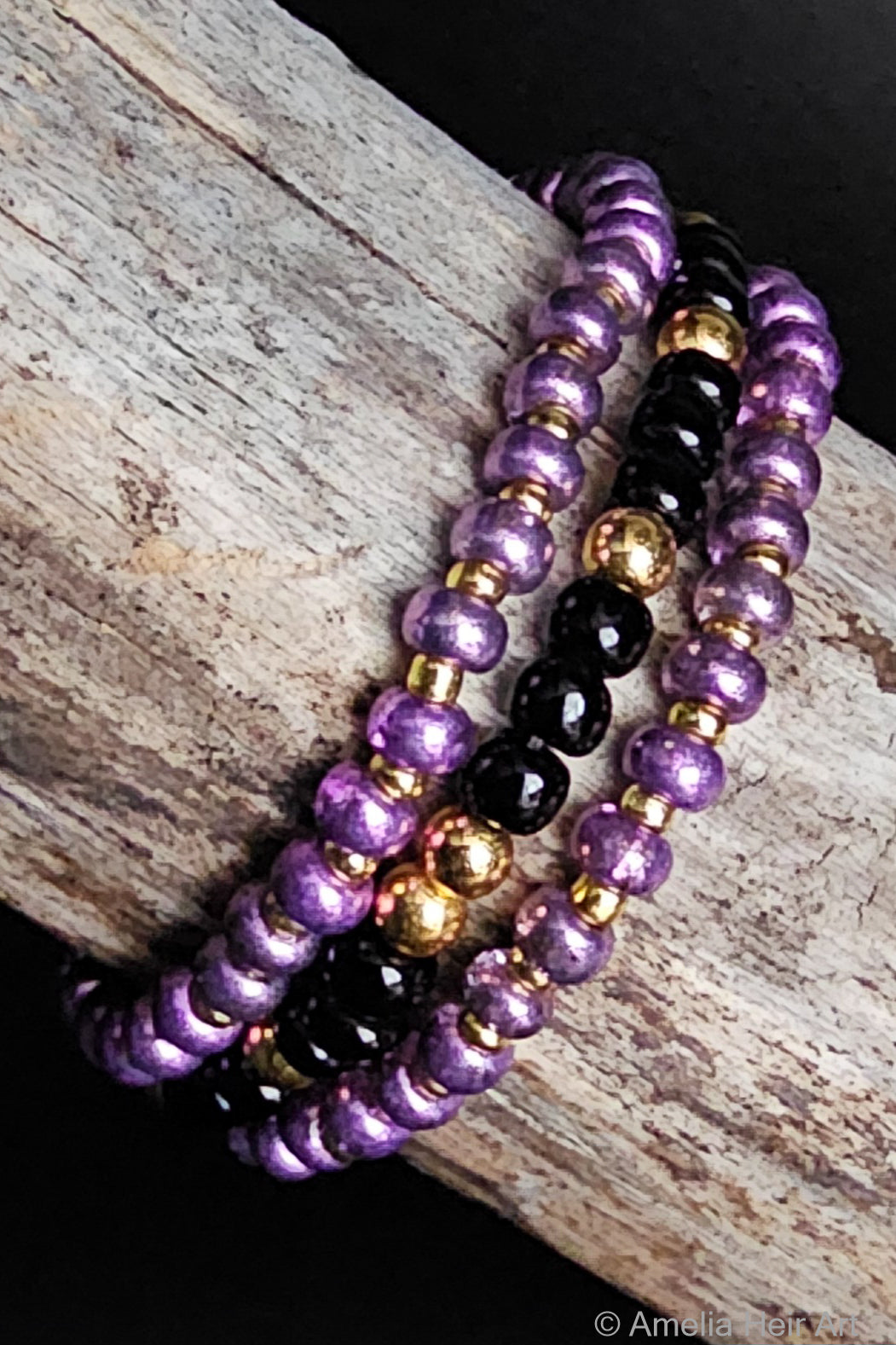 Three beaded bracelets in purple, black, and gold on a wooden surface.
