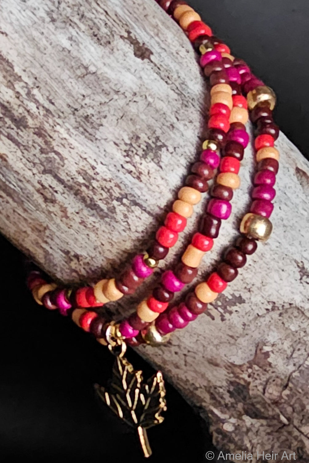 Multicolored beaded bracelet with a gold leaf charm on a wood surface