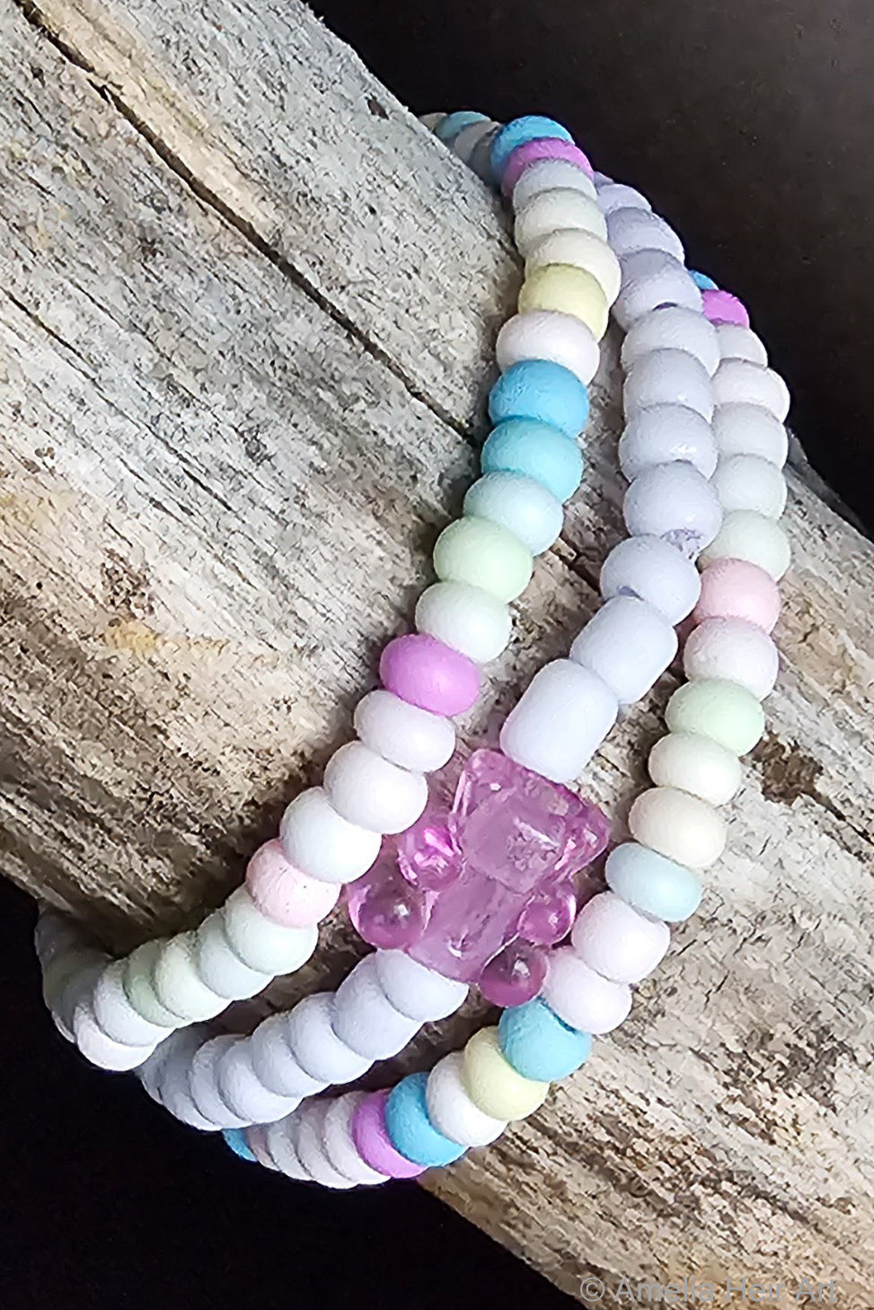 Set of pastel beaded bracelets with a pink gummy-bear-shaped bead on a wooden surface