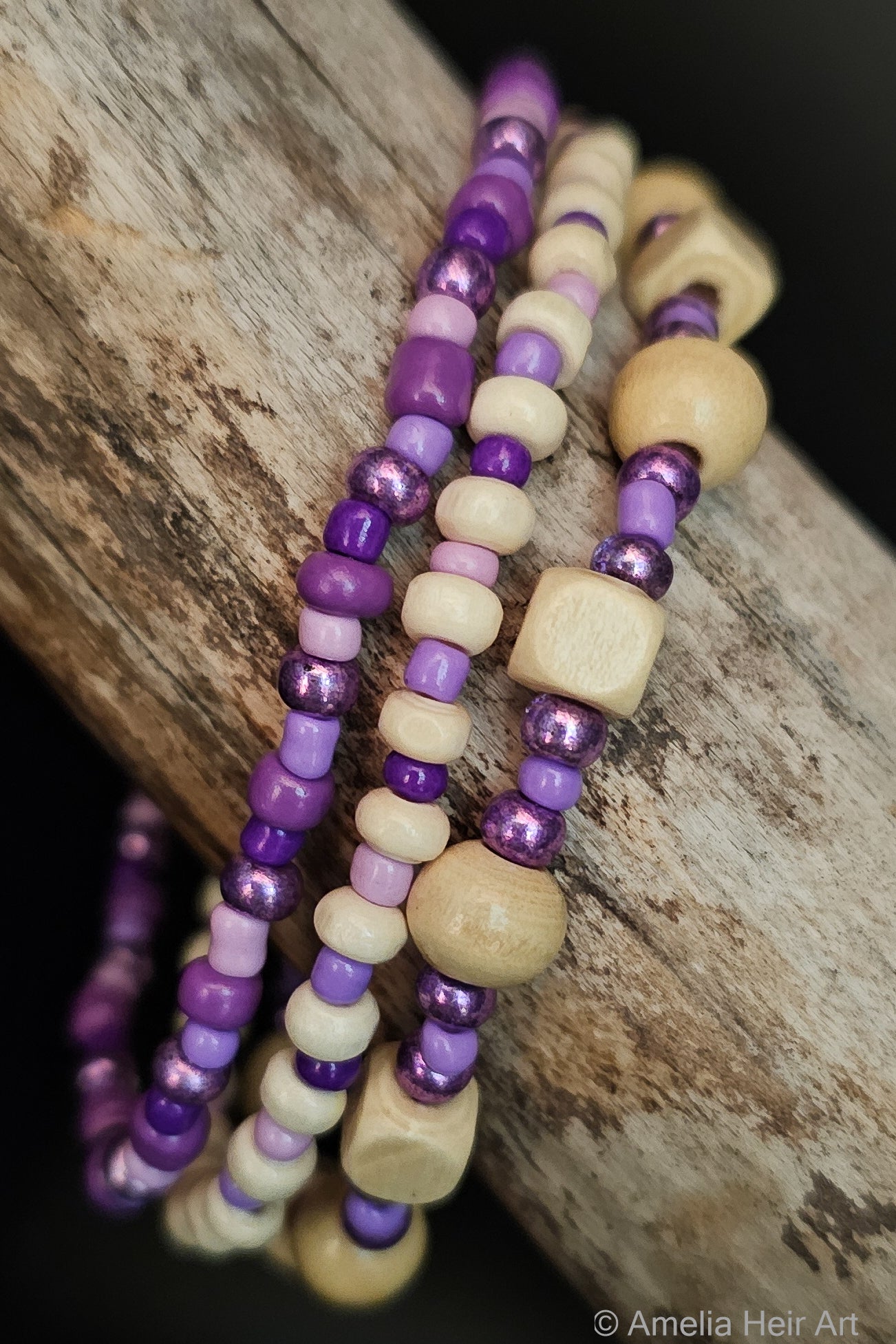 Three beaded bracelets with purple and cream beads on a wooden surface.