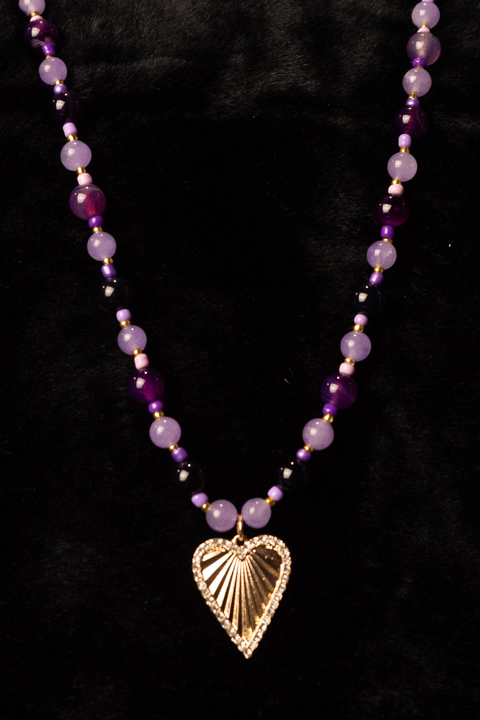 Necklace with purple beads and a gold heart-shaped pendant on a black background