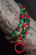 Colorful beaded bracelet with red, green, and gold beads with a red circle charm on a wooden surface.