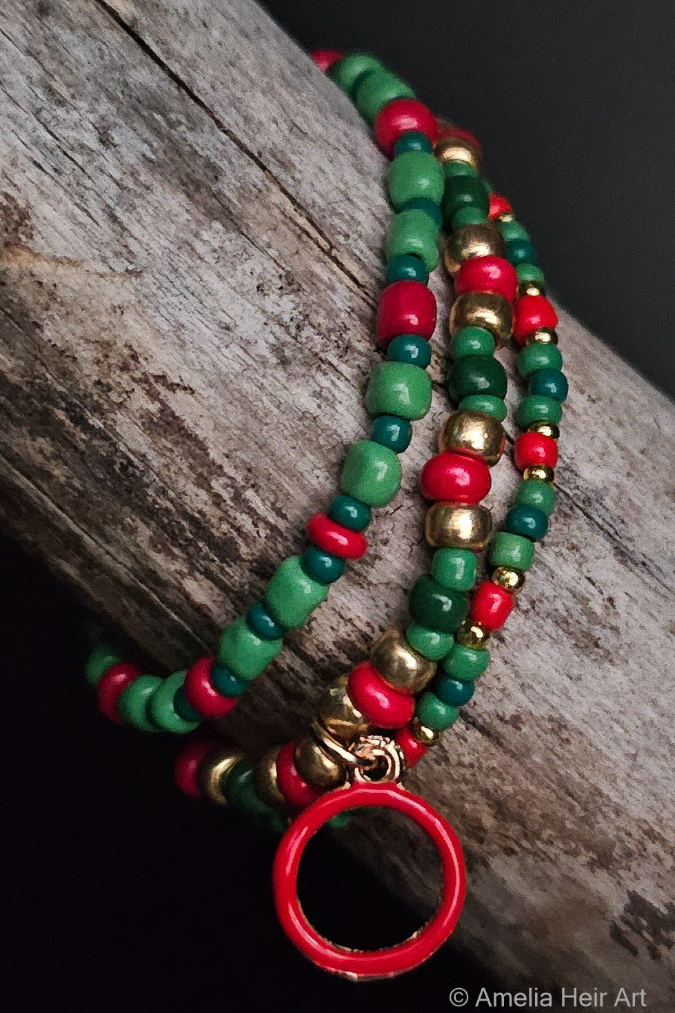 Colorful beaded bracelet with red, green, and gold beads with a red circle charm on a wooden surface.
