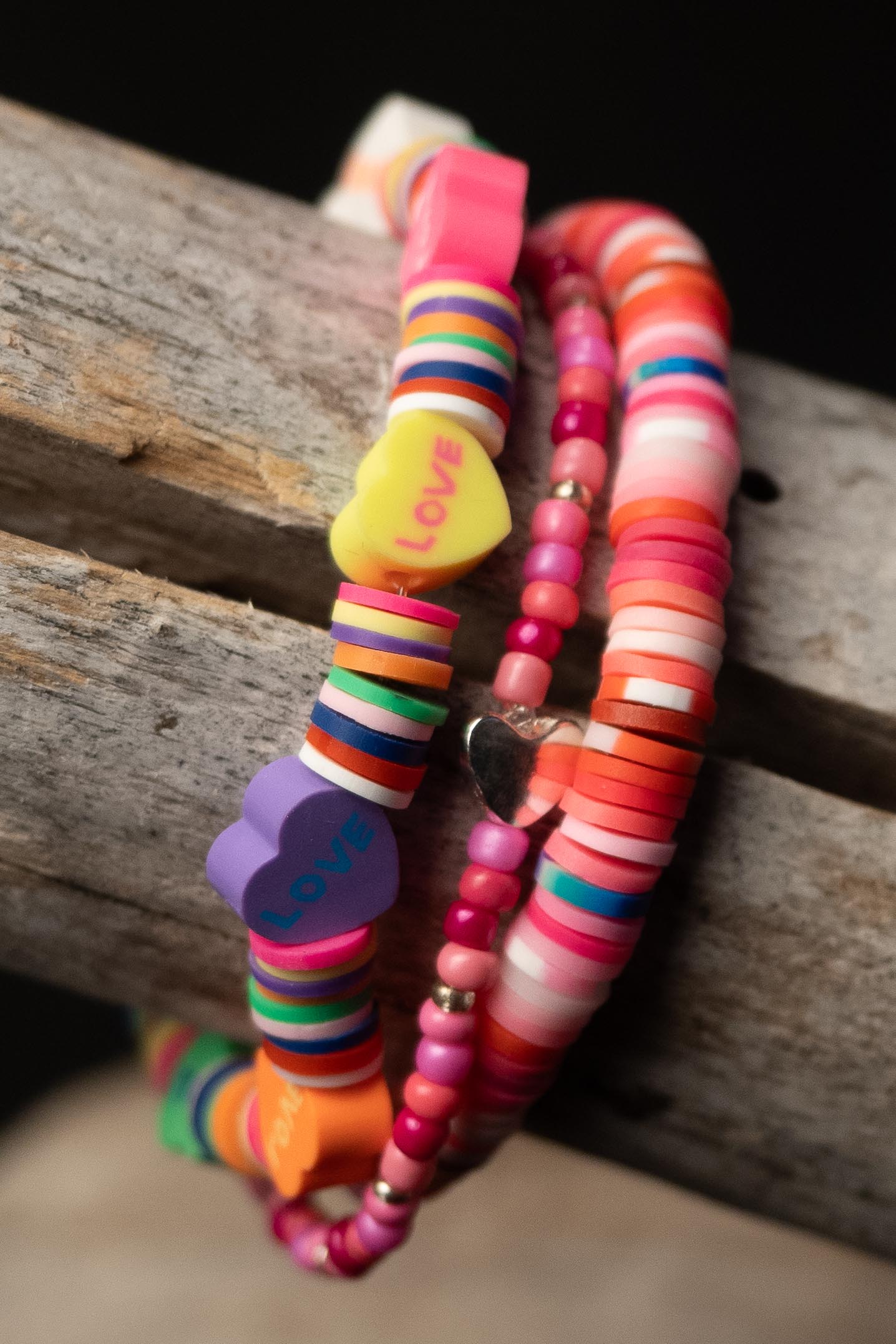 Colorful beaded bracelets with 'LOVE' heart-shaped beads on a wooden surface
