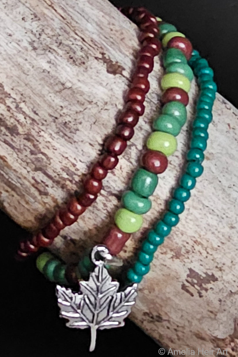 Green and brown beaded bracelets with a silver leaf charm on a wooden surface