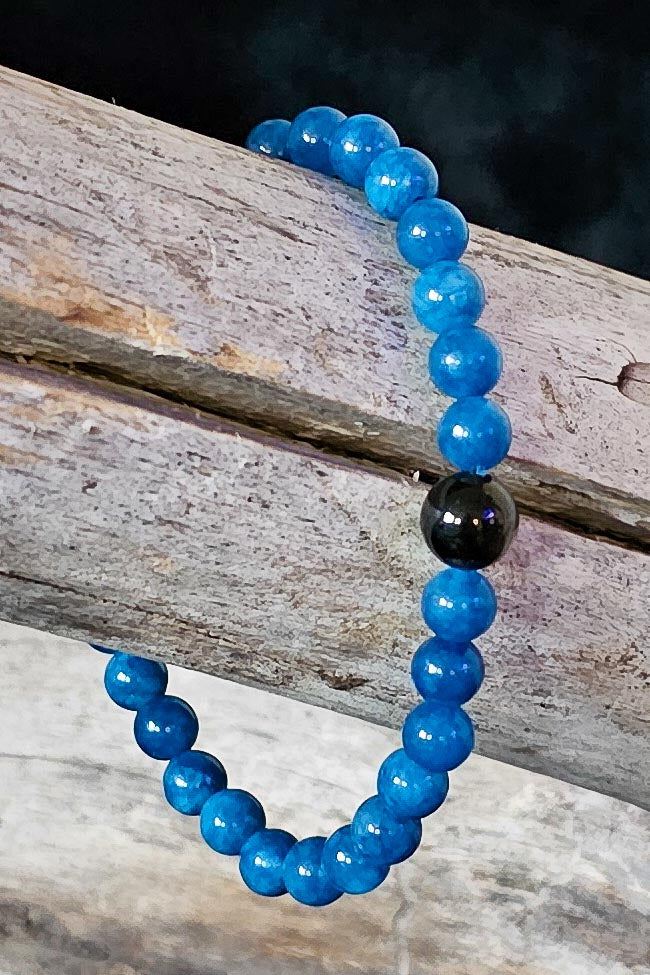 Blue beaded bracelet with a black bead on a wooden surface