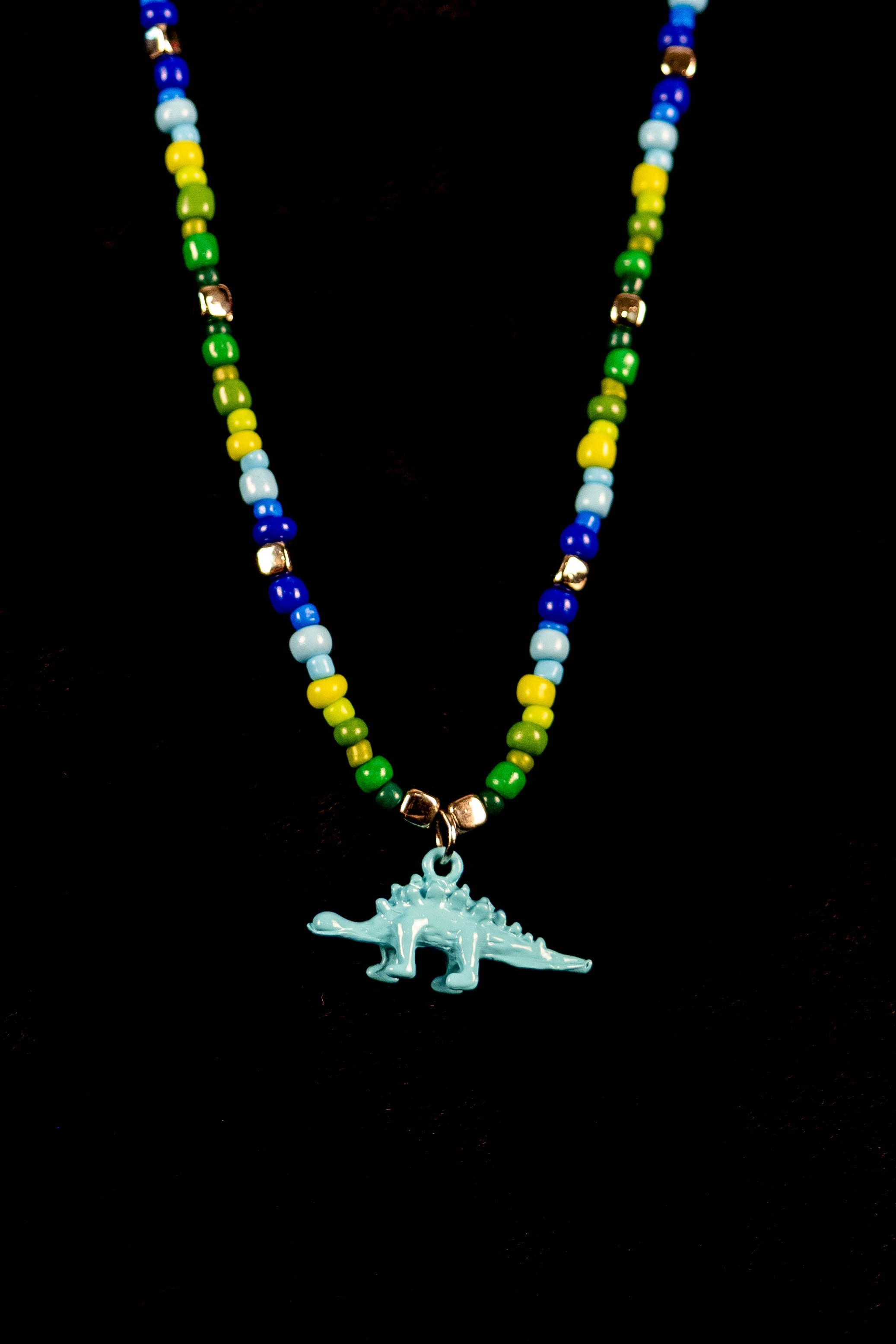 Necklace with colorful beads and a blue dinosaur charm on a black background