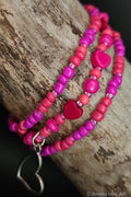 Three pink beaded bracelets with a silver heart charm on a wooden surface