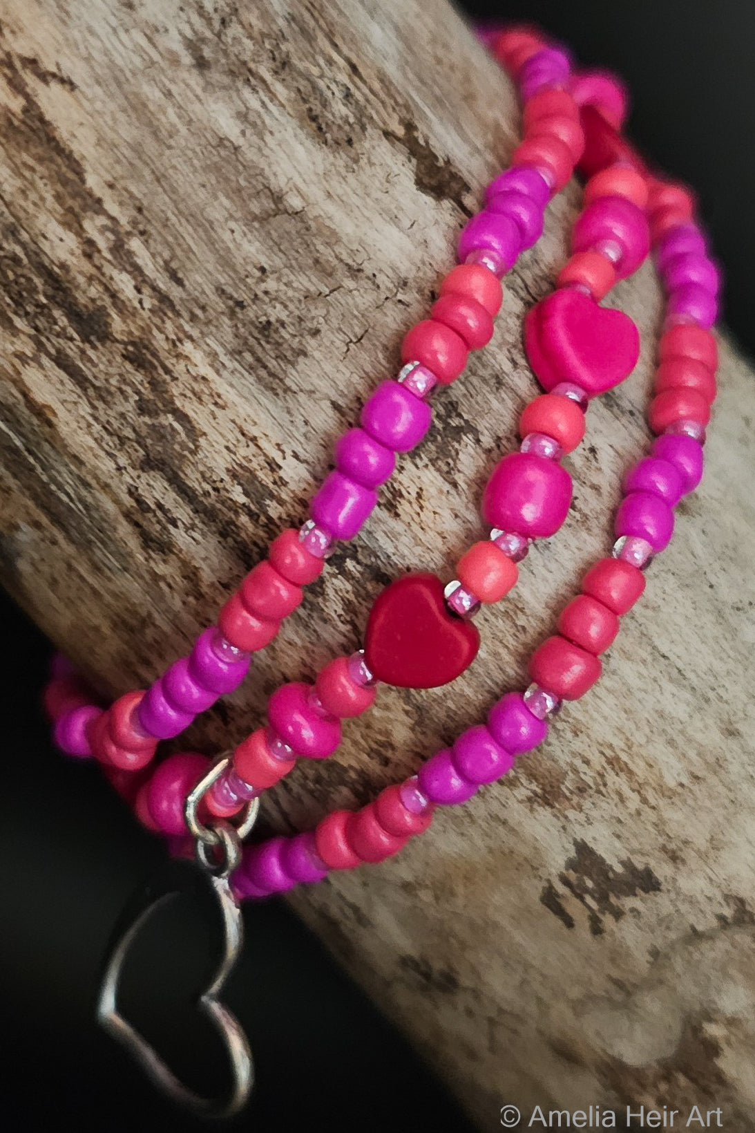 Three pink beaded bracelets with a silver heart charm on a wooden surface