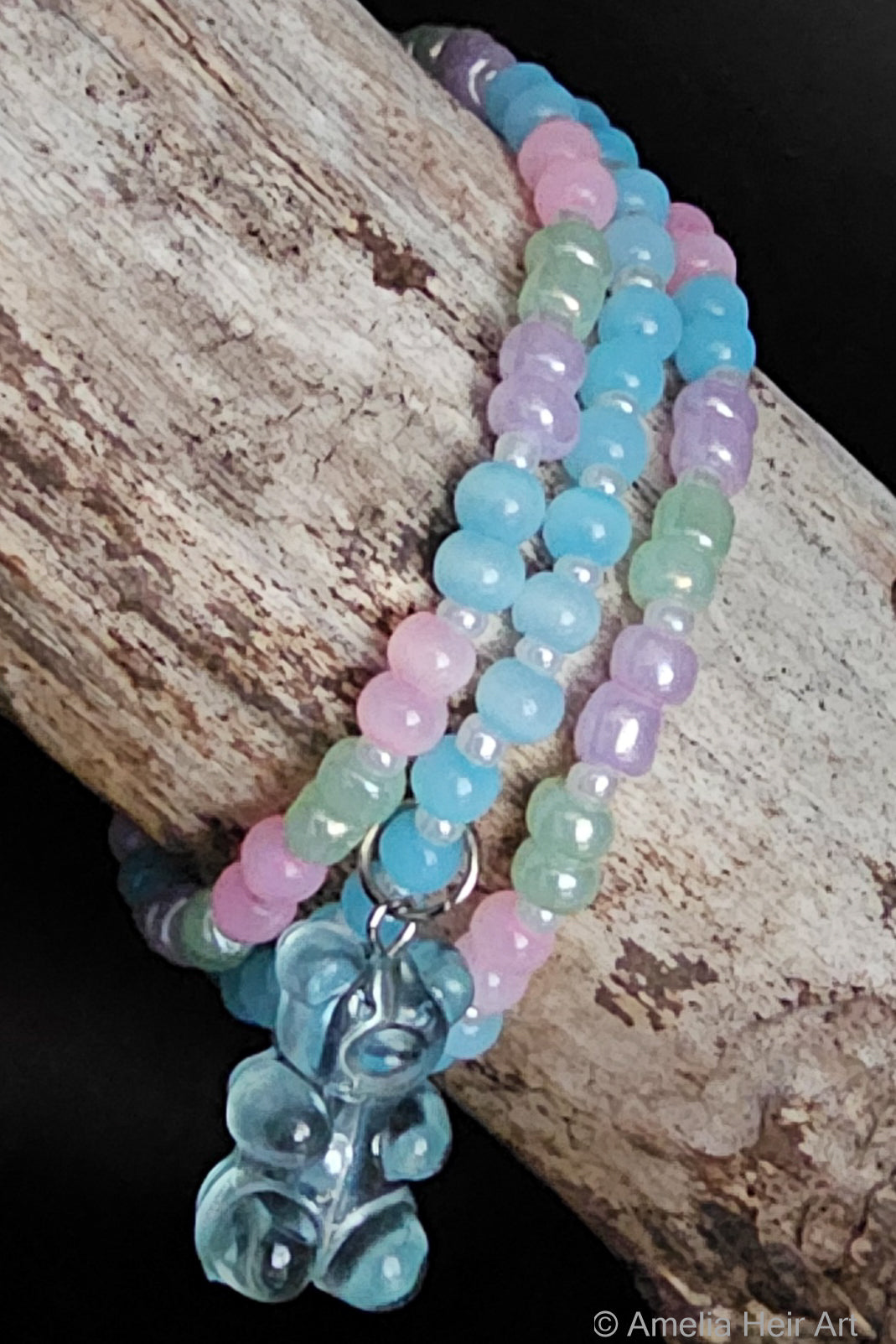 Multicolored beaded bracelets with a gummy-bear-shaped charm on a wooden surface