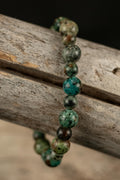 Beaded bracelet with varying greens and browns on a wooden surface