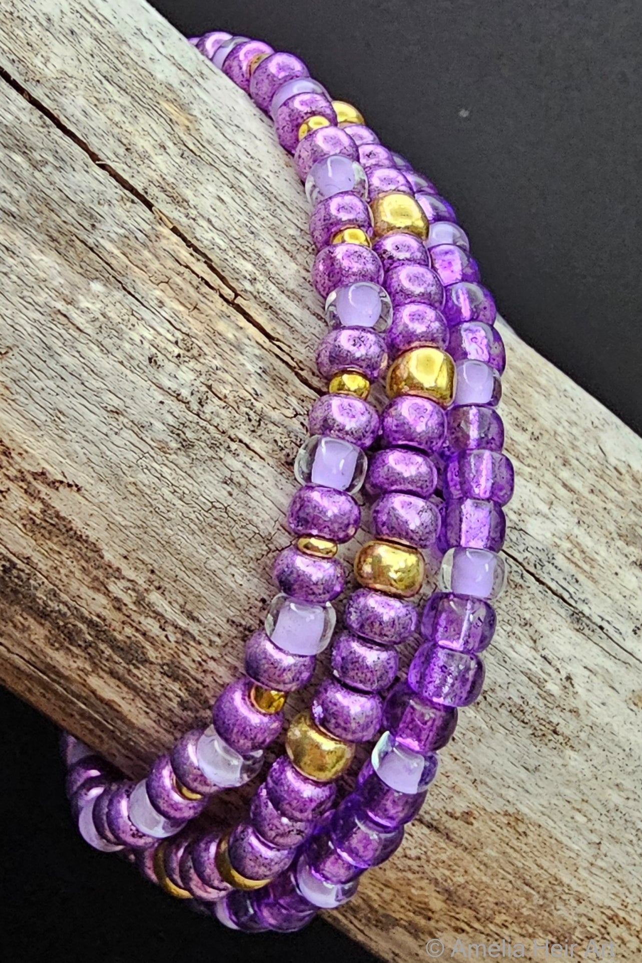 Purple beaded bracelet with gold accents on a wooden surface