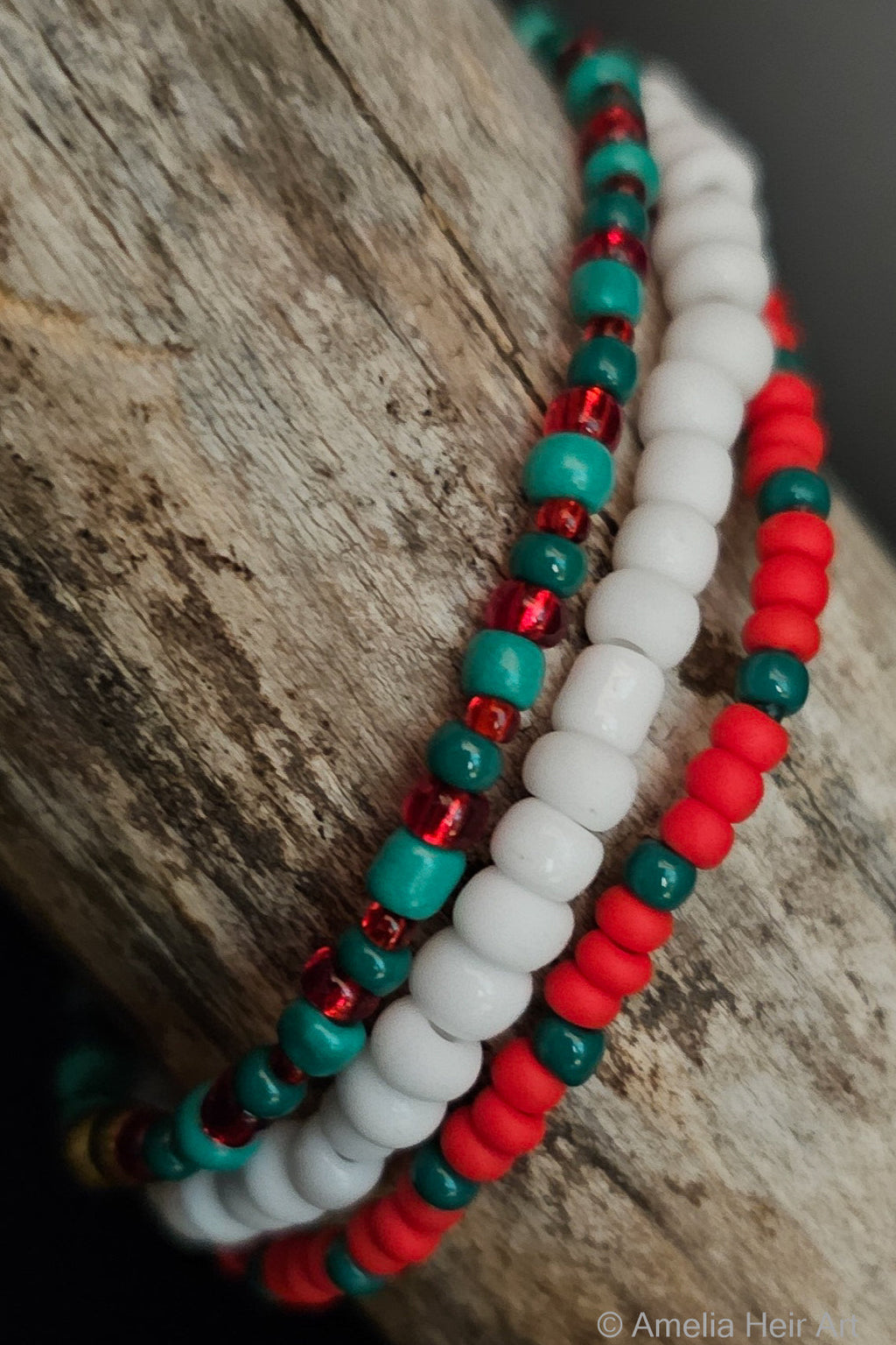 Three beaded bracelets in red, green, and white on a wooden surface.