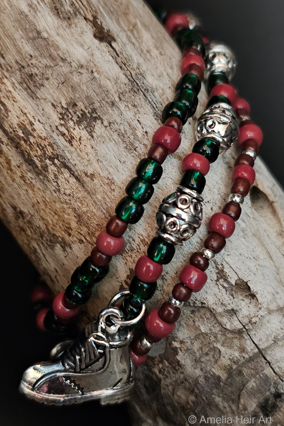 Three beaded bracelets with a silver hiking boot charm on a wooden surface