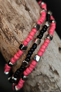 Three beaded bracelets in pink, black, and silver on a wooden surface.