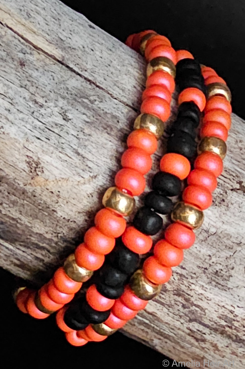 Three beaded bracelets in pink, black, and gold on a wooden surface.