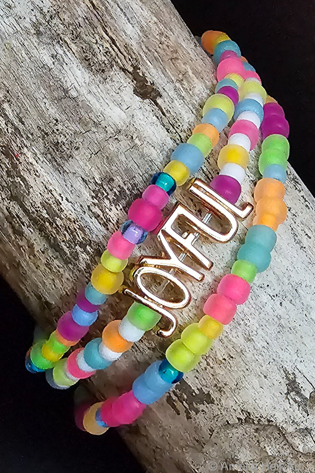 Joyful Beaded Bracelet handcrafted full-spectrum fluorescent beaded bracelet with JOYFUL charm on a wooden surface — Amelia Heir Art