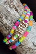 Colorful fluorescent beaded bracelet with 'JOYFUL' charm on a wooden surface