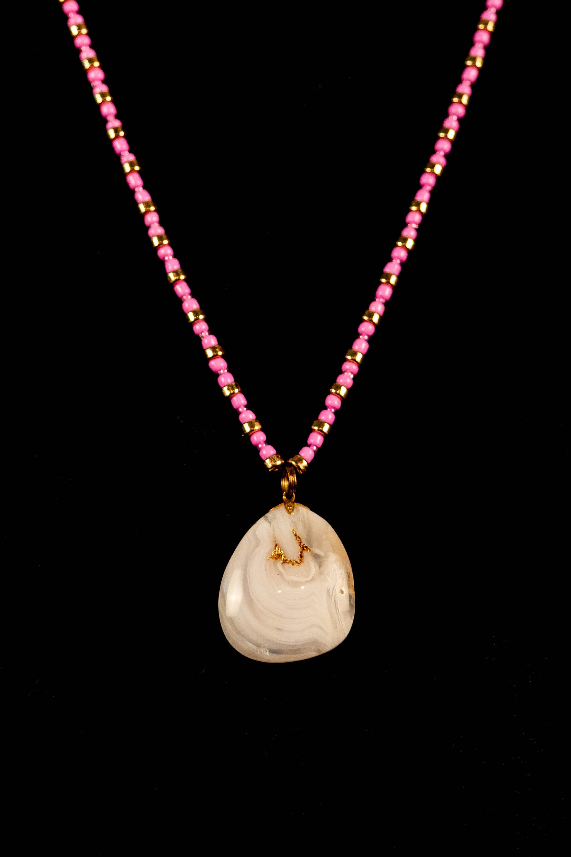 Necklace with a white stone pendant and pink bead chain on a black background