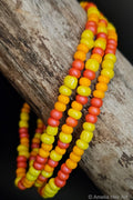 Three beaded bracelets in yellow, orange, and pink on a wooden surface