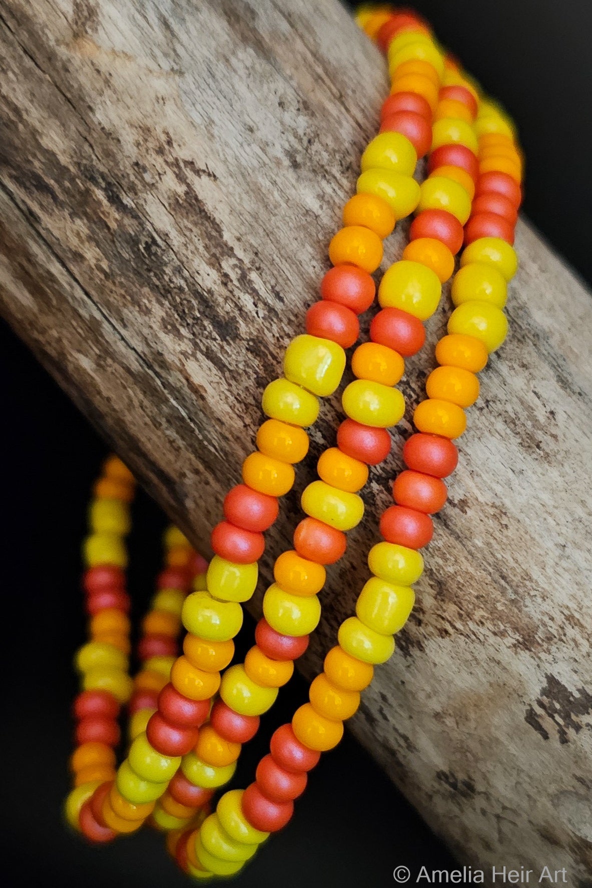 Three beaded bracelets in yellow, orange, and pink on a wooden surface
