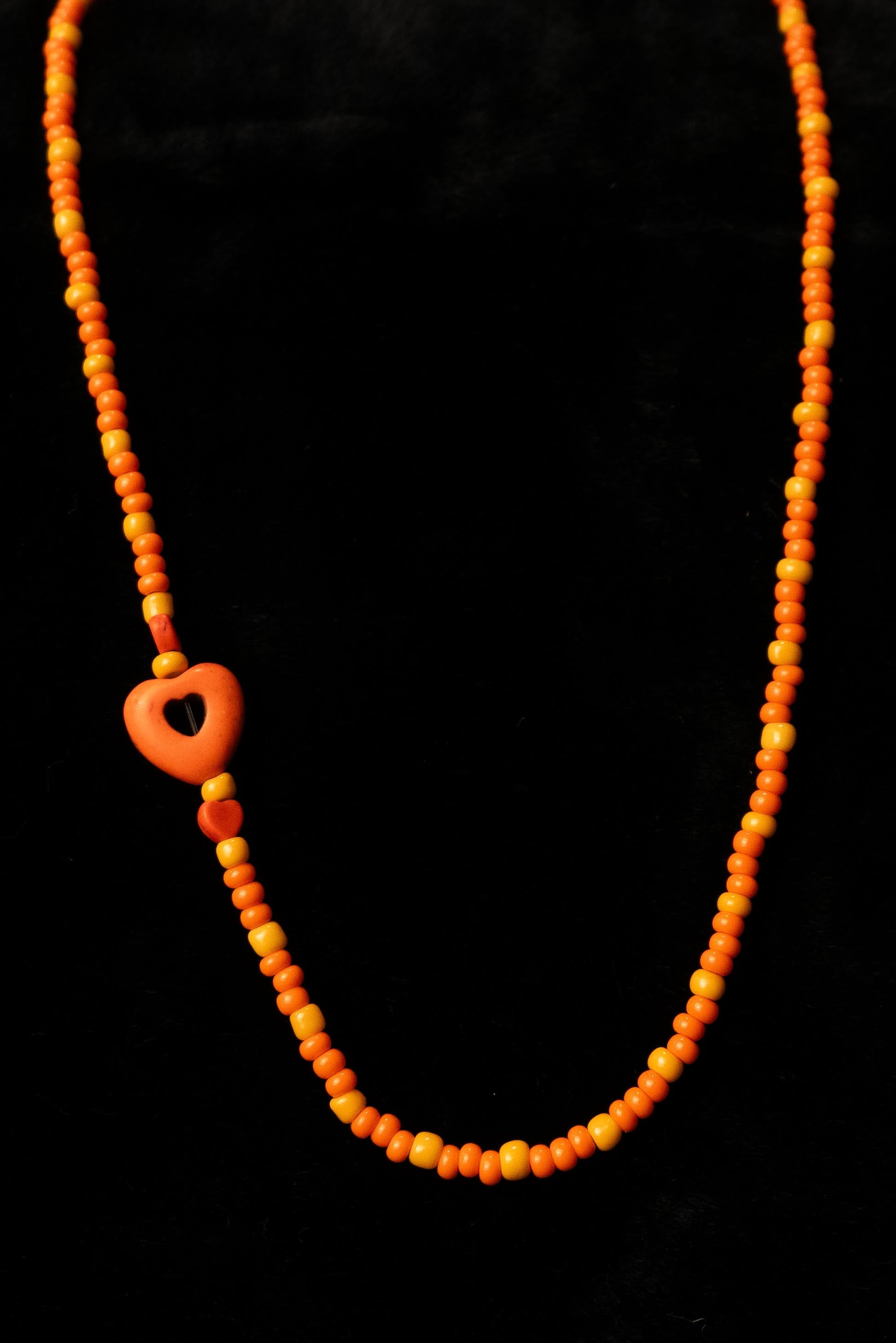 Necklace with orange beads and a heart-shaped bead on a black background